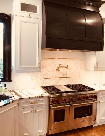 A kitchen with white cabinets and black hood