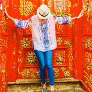 A woman in blue jeans and white hat standing next to red wall.